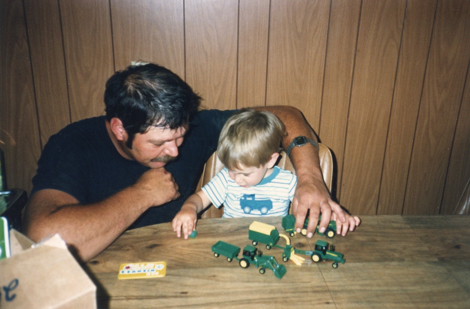 Ben as a small boy and his dad at the table, playing with toy John Deere farm equipment.