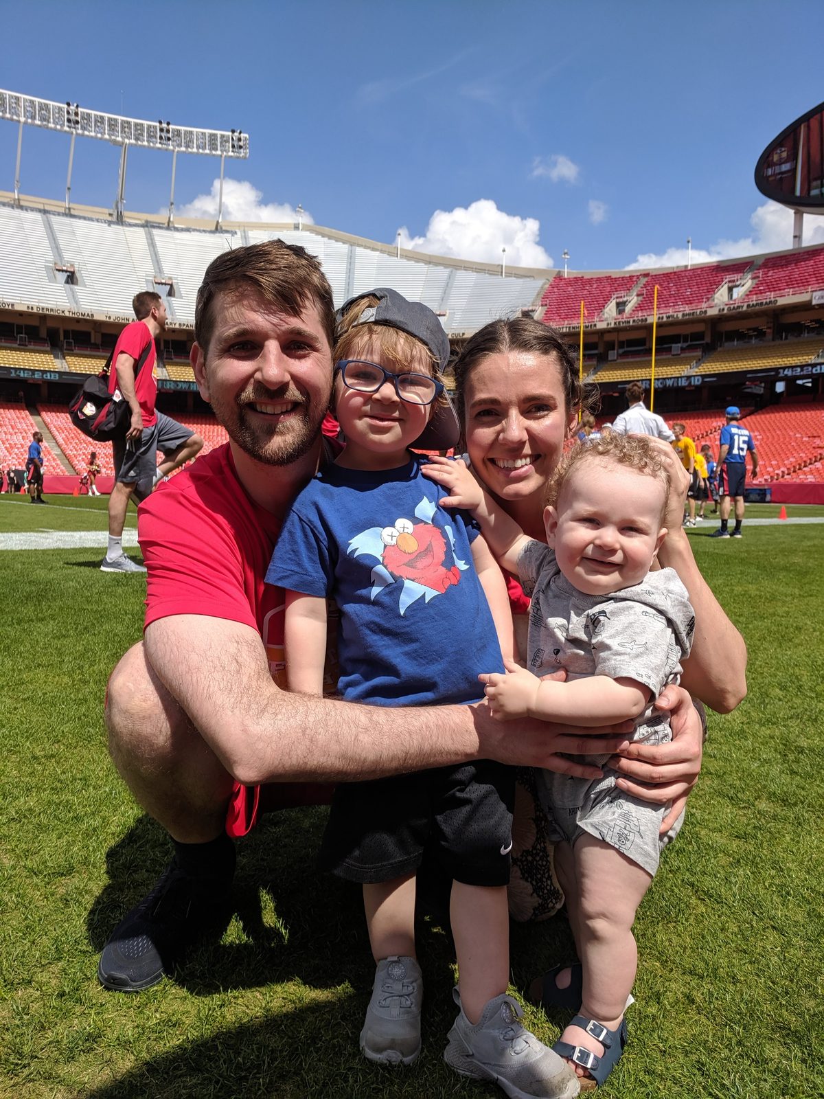 Ben, Hannah, and their two young sons together on the Arrowhead field under a blue sky.